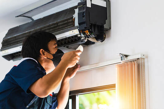 A male technician in Greenwich, CT repairs and maintains air conditioners.